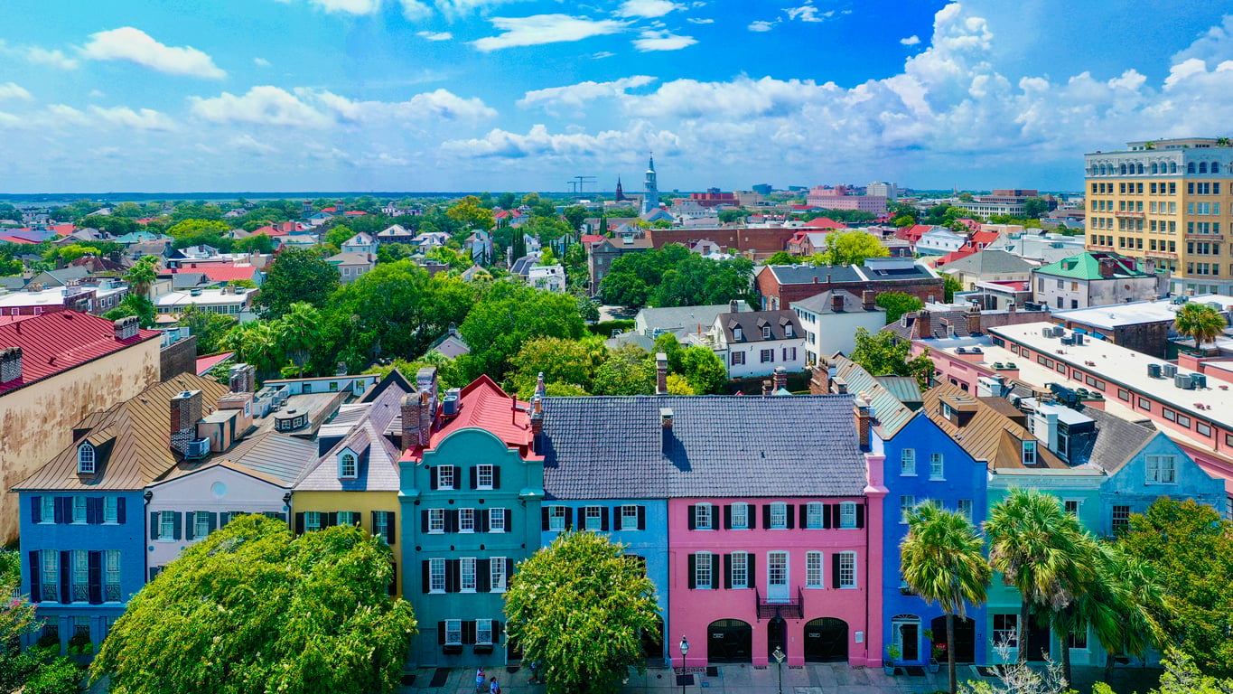 Aerial view of the colorful historic houses of Rainbow Row in Charleston, South Carolina, with the city skyline in the distance.