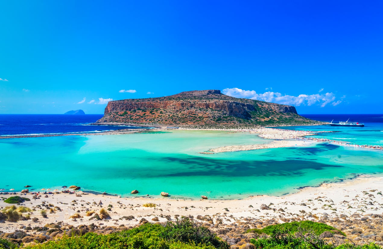 Turquoise shallow water at Balos Beach in Crete, with a large rocky island in the background.