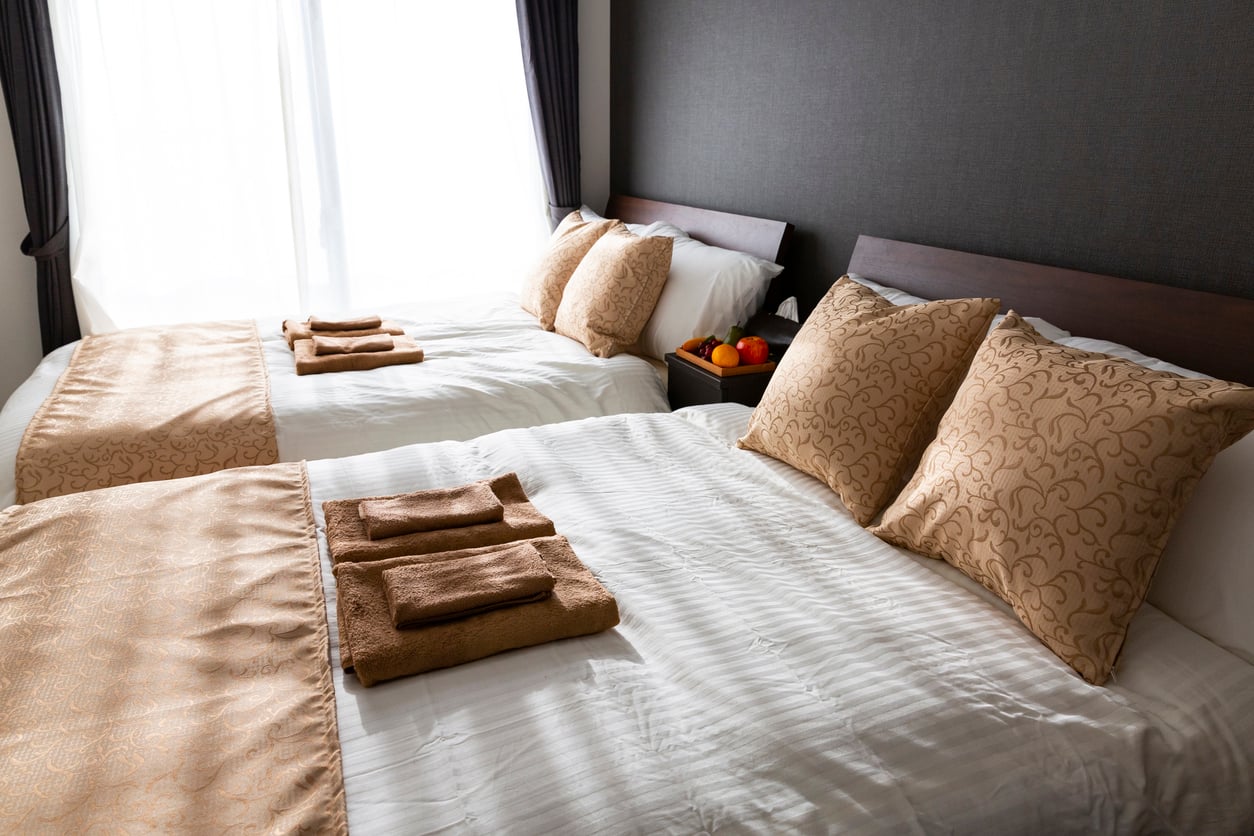 Two hotel beds with white linens, patterned pillows, and folded brown towels, perfect for those making trip planning decisions.