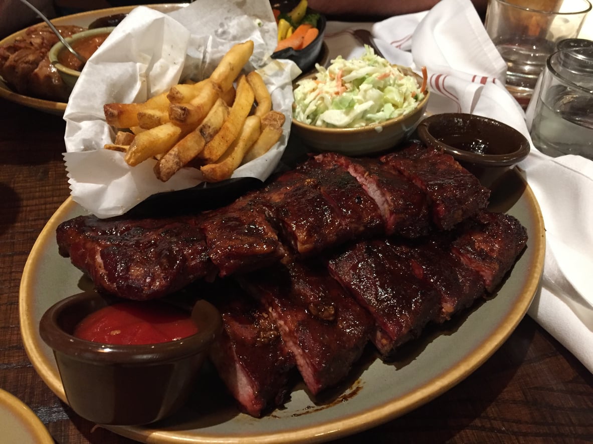 A plate of barbecue ribs served with a basket of french fries, coleslaw, and dipping sauces.