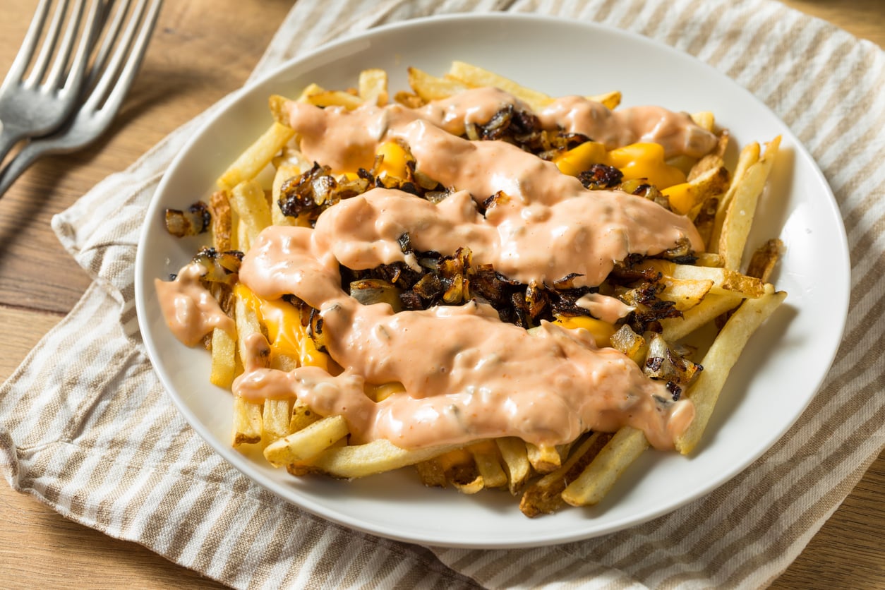 restaurants where the side dish French fries topped with melted cheese, caramelized onions, and a creamy orange sauce on a white plate.