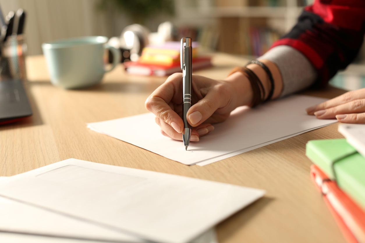 A person writes on a blank sheet of paper with a silver pen at a desk.