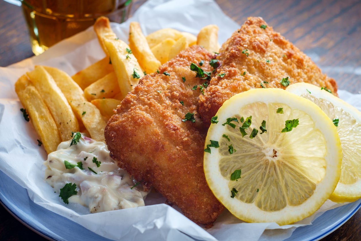 Fish and chips with a side of tartar sauce, garnished with parsley and lemon slices.