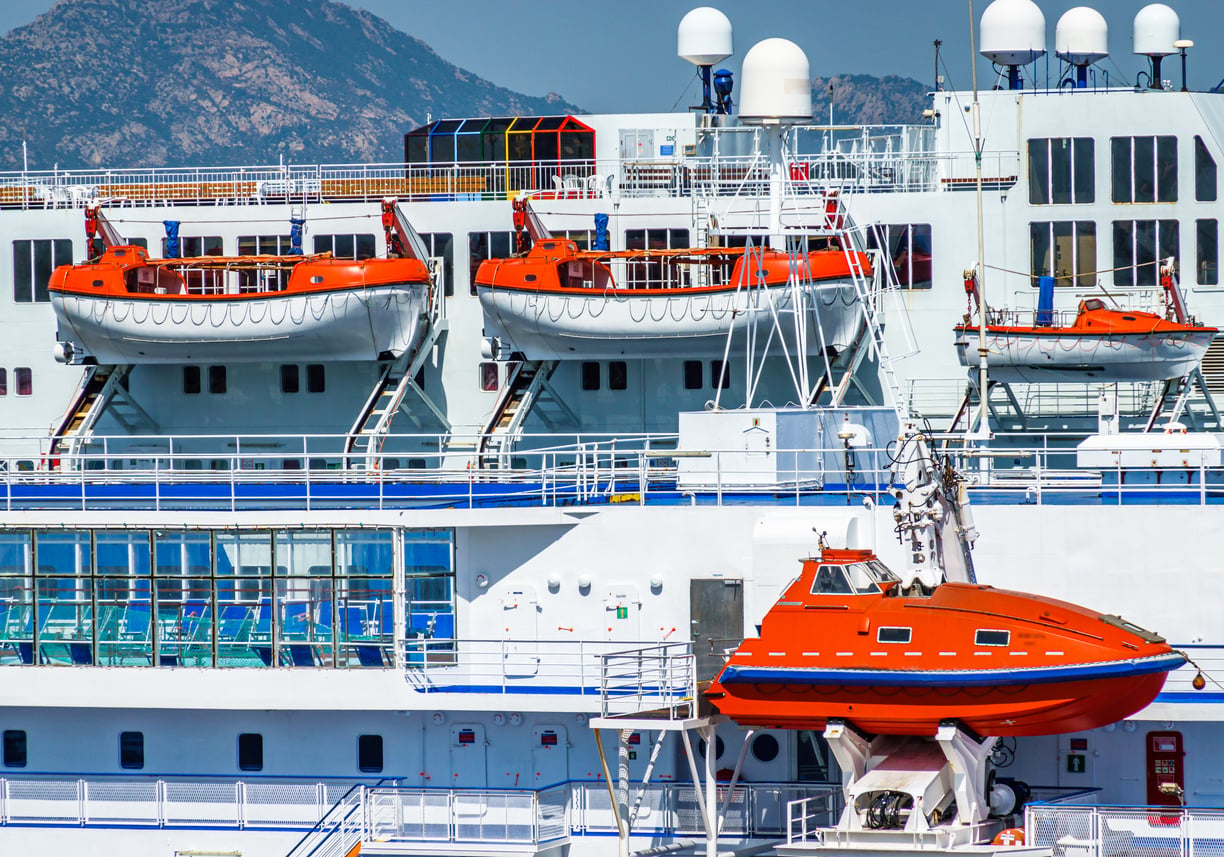 A white cruise ship featuring multiple orange lifeboats stored along its decks.