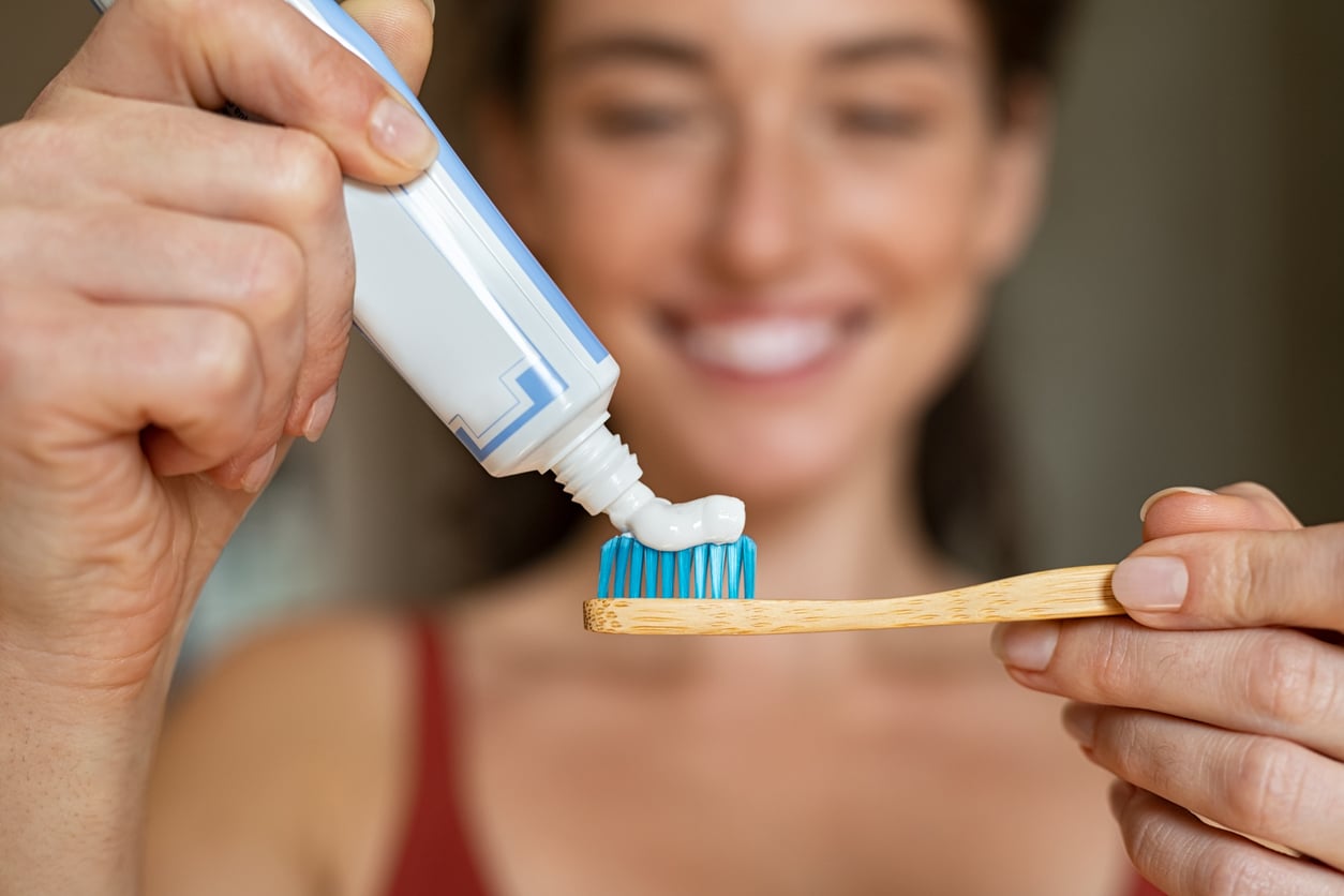 A person squeezing toothpaste onto a bamboo toothbrush.
