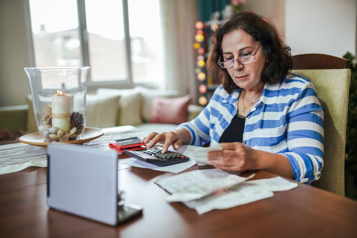 A woman sitting at a table using a calculator and reviewing receipts.
