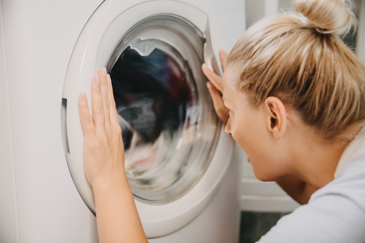 A woman leaning in to watch clothes spinning inside a washing machine.