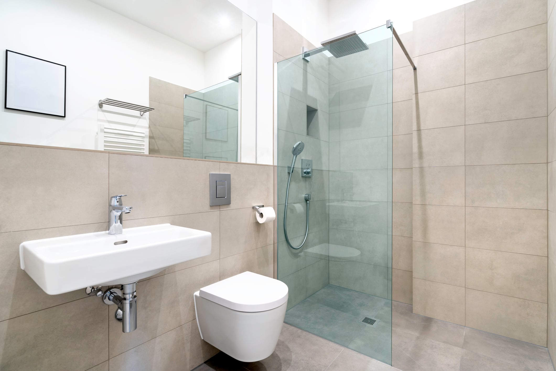 A modern bathroom renovation featuring a wall-mounted sink, a wall-hung toilet, and a glass-enclosed walk-in shower with beige tiled walls, showcasing quality home improvements.