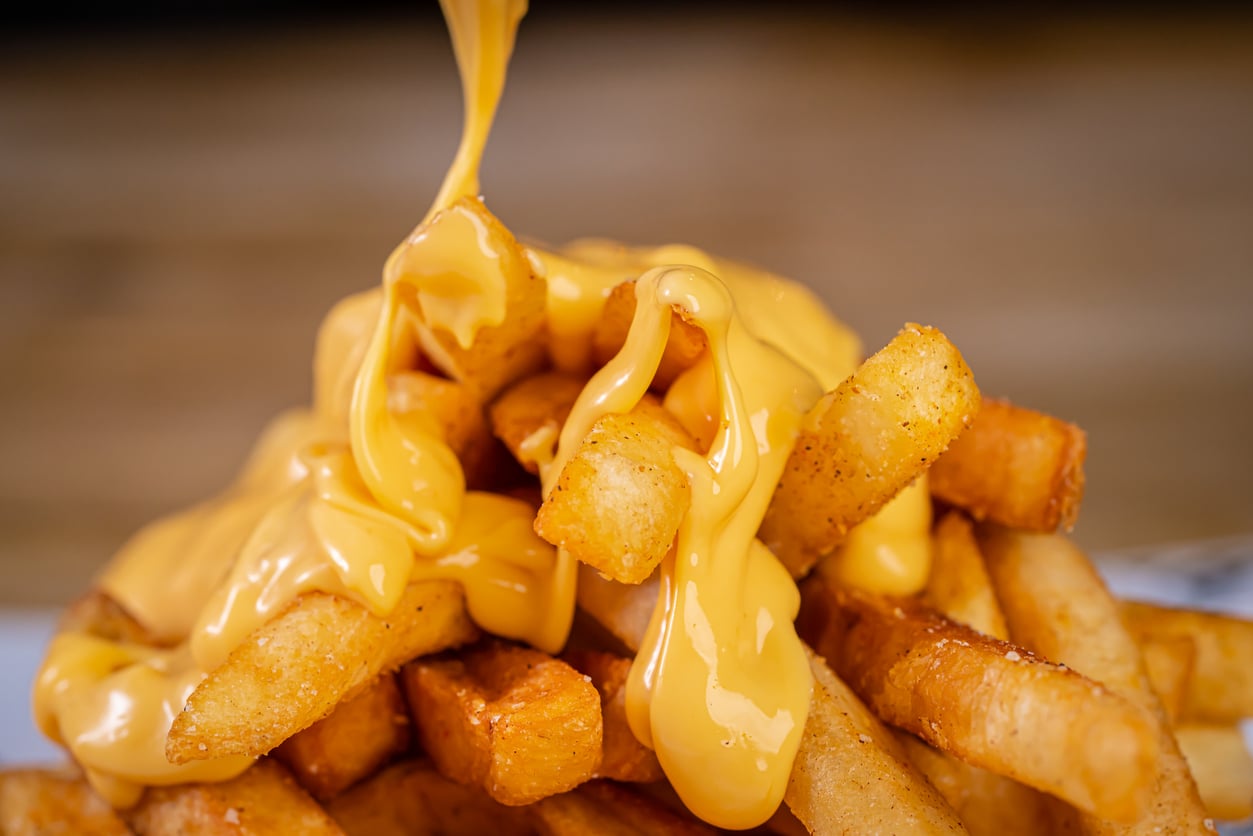 Warm cheese sauce being poured over a pile of golden french fries.
