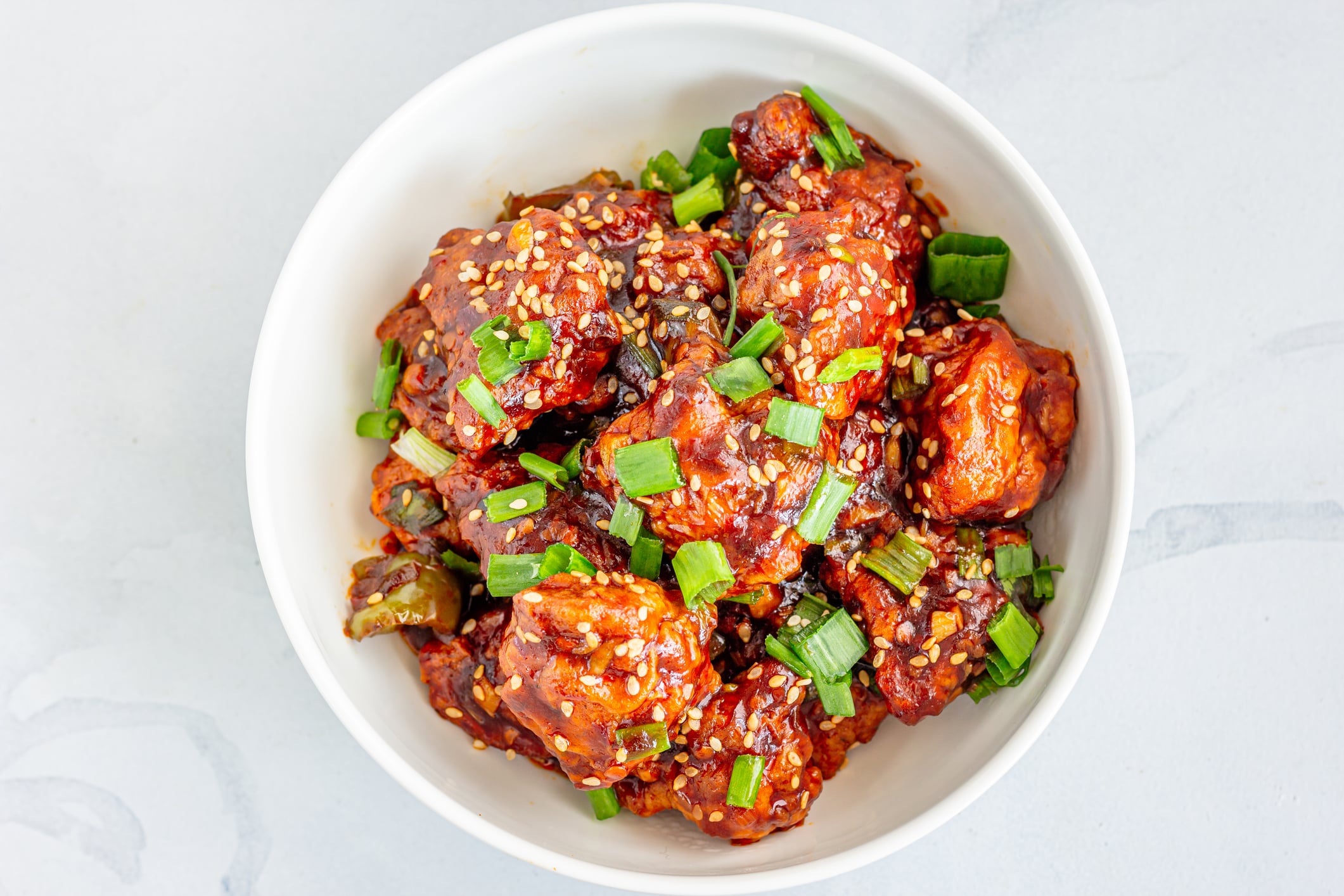 A bowl of Gobi Manchurian topped with sesame seeds and chopped green onions.