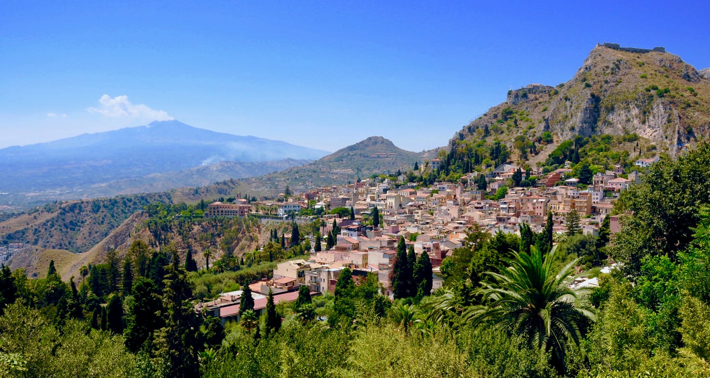 The town of Taormina nestled on a hillside in Sicily, with Mount Etna visible in the background.