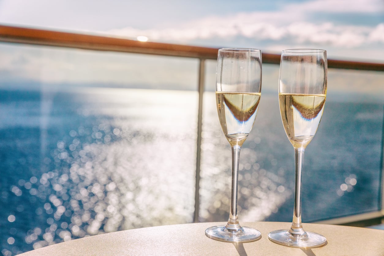 Two champagne flutes filled with sparkling wine sit on a table overlooking the ocean.