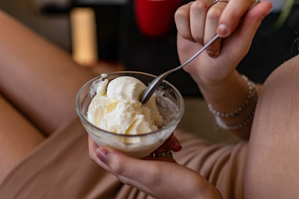 A person holding a glass bowl of vanilla ice cream and a spoon.