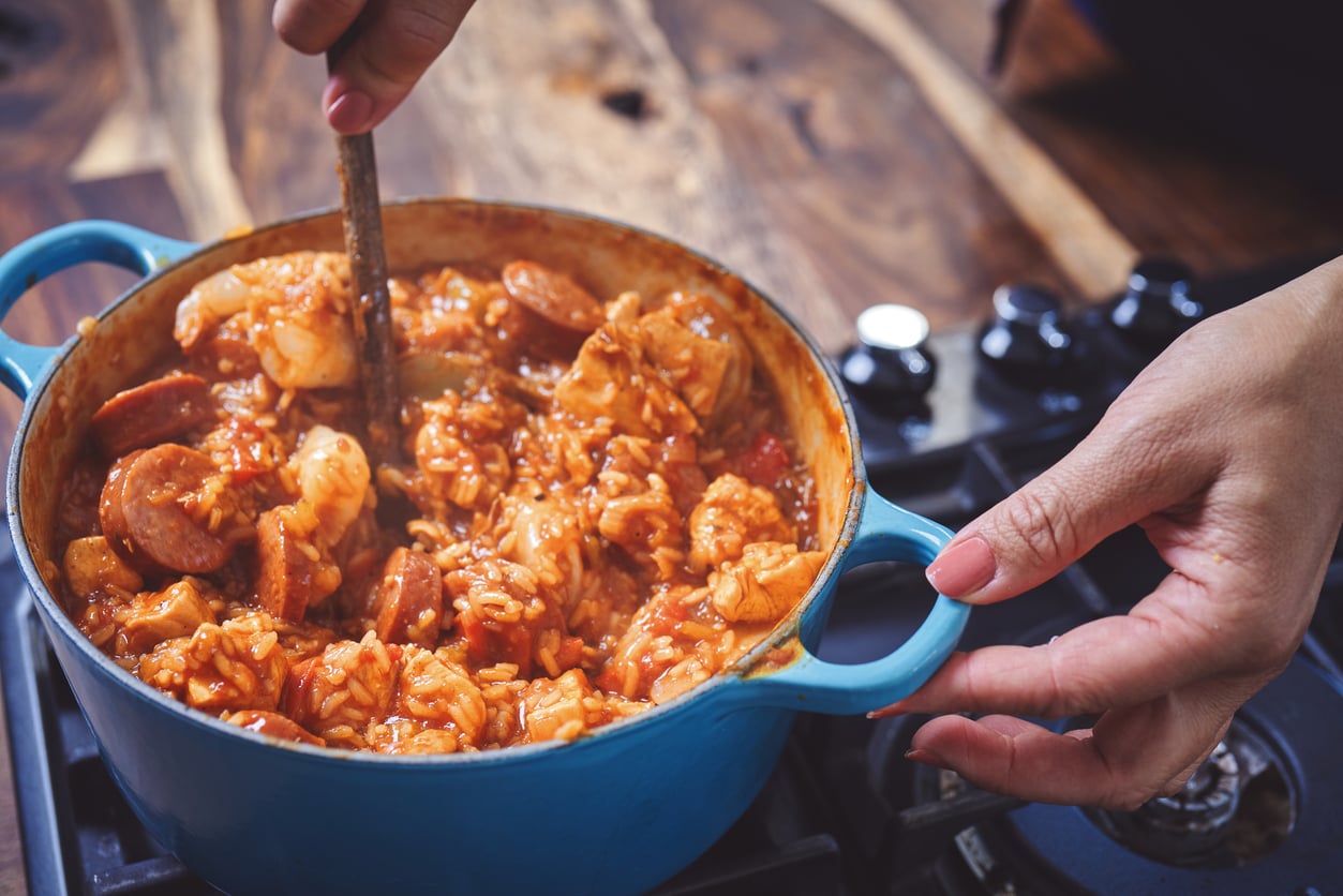 Hands stirring a blue pot of jambalaya on a stovetop.