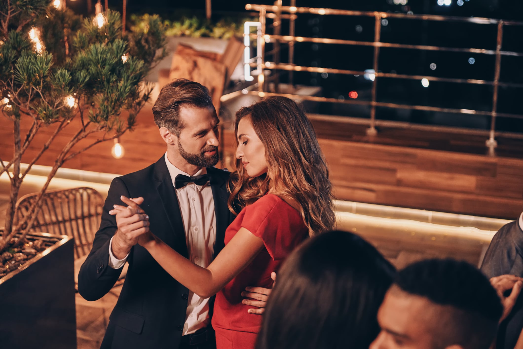 A man in a tuxedo and a woman in a red dress dancing together at an evening event.