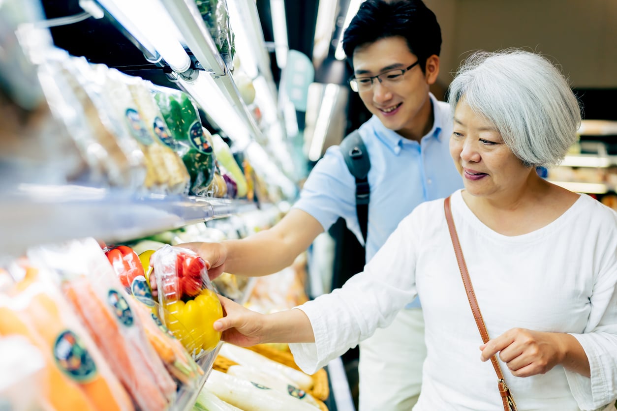 An older woman and a young man shopping for produce in a grocery store.