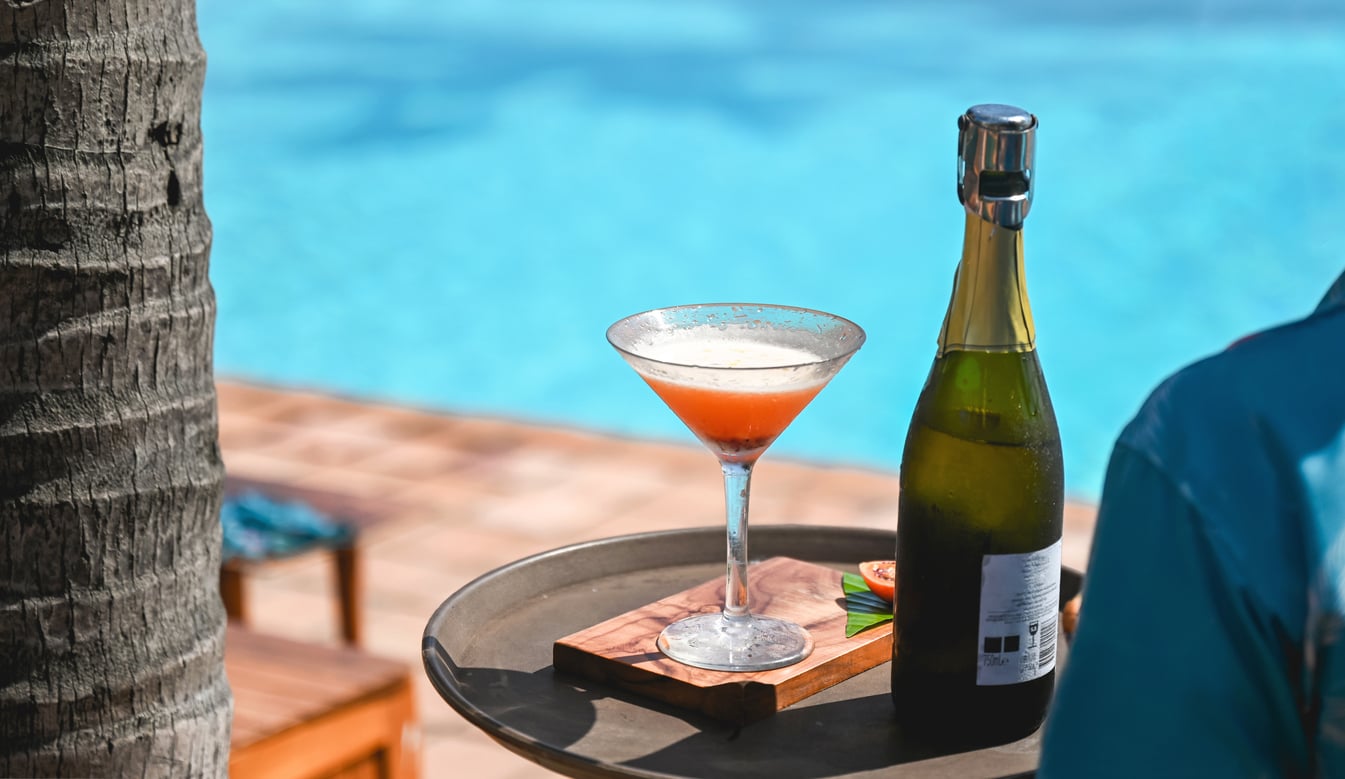 A martini glass and a bottle of sparkling wine on a tray by a swimming pool, representing typical cruise ship charges.