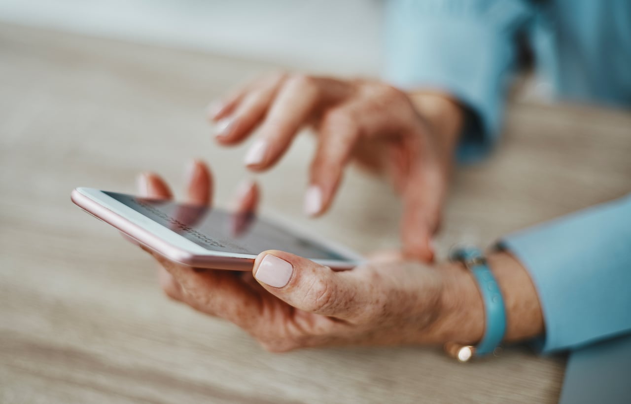 Close-up of a person’s hands using a smartphone on a wooden surface.