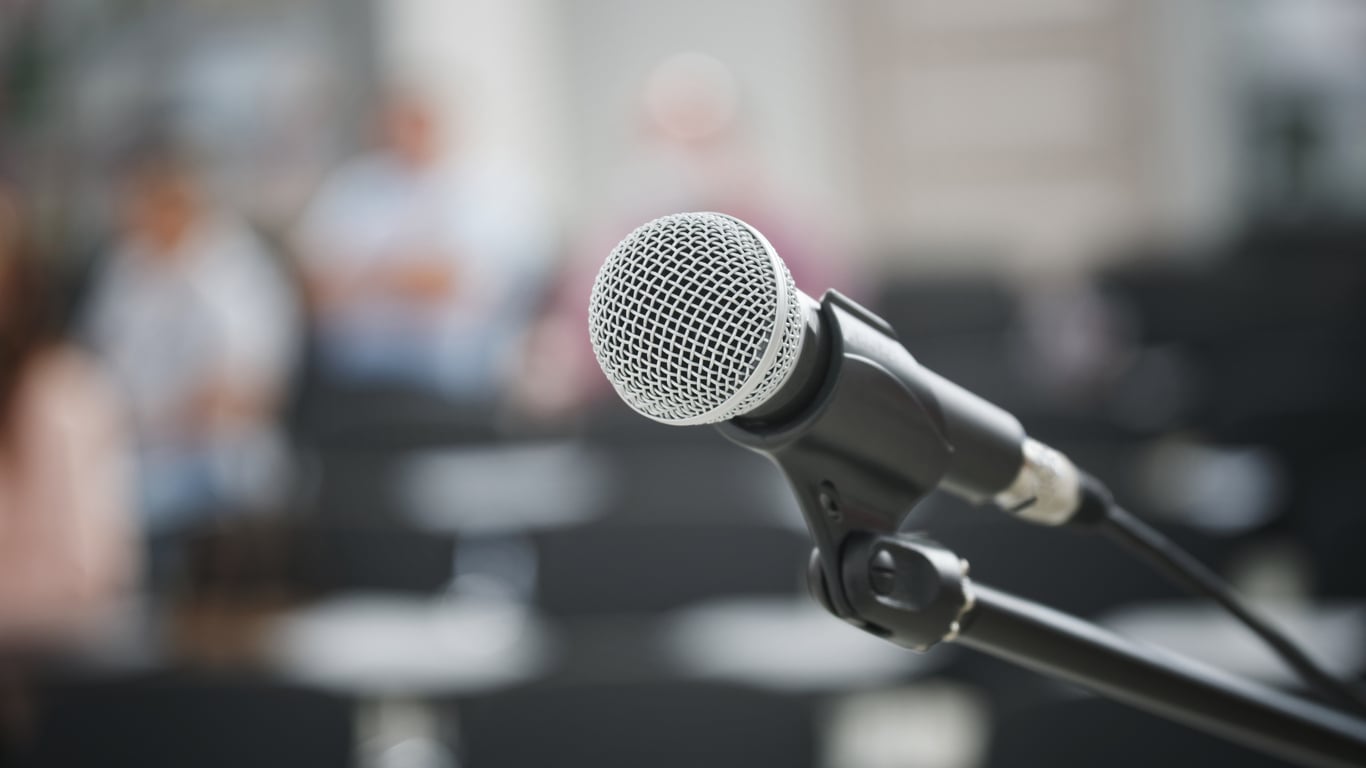 A microphone on a stand in front of a blurred audience.