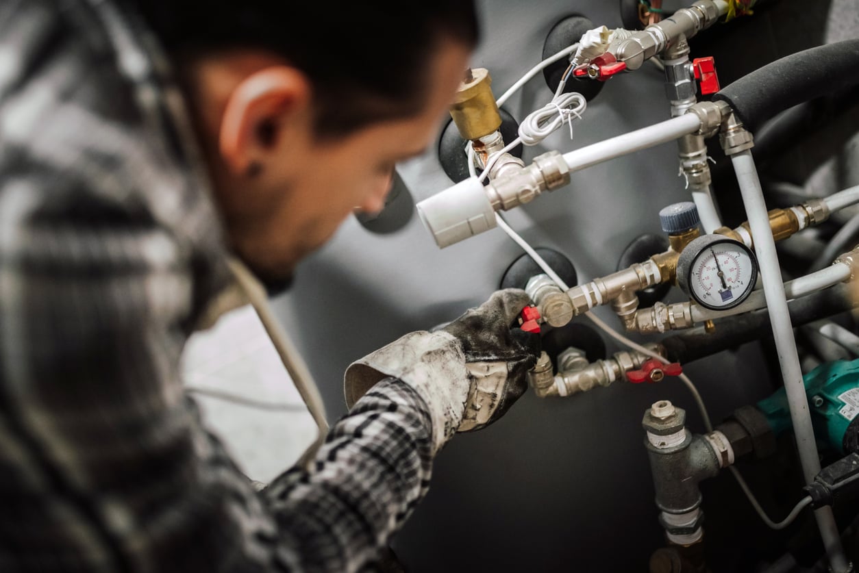 A technician in work gloves adjusts a valve on a residential heating system.