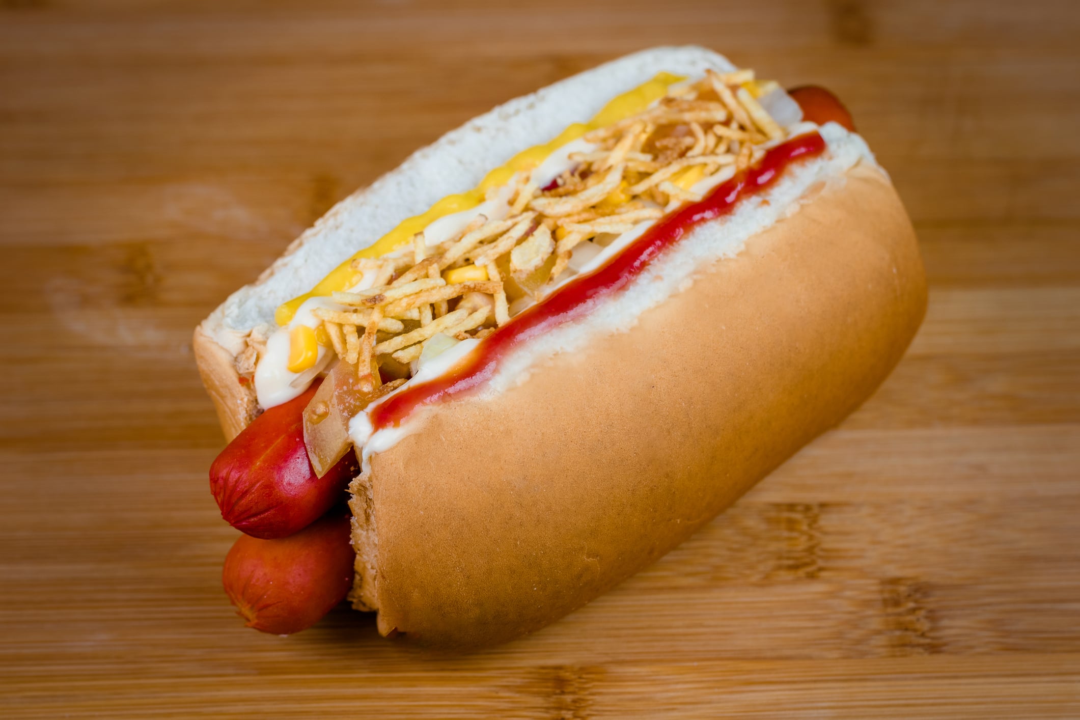 A hot dog in a bun topped with ketchup, mustard, and crispy shoestring potatoes.