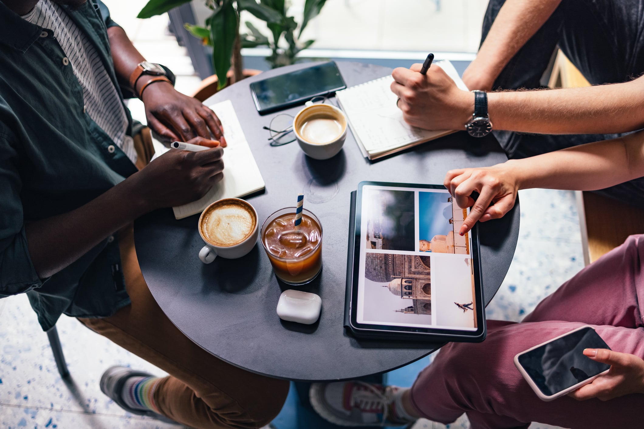 Three people sitting around a round table writing in notebooks and viewing architectural photos on a tablet.