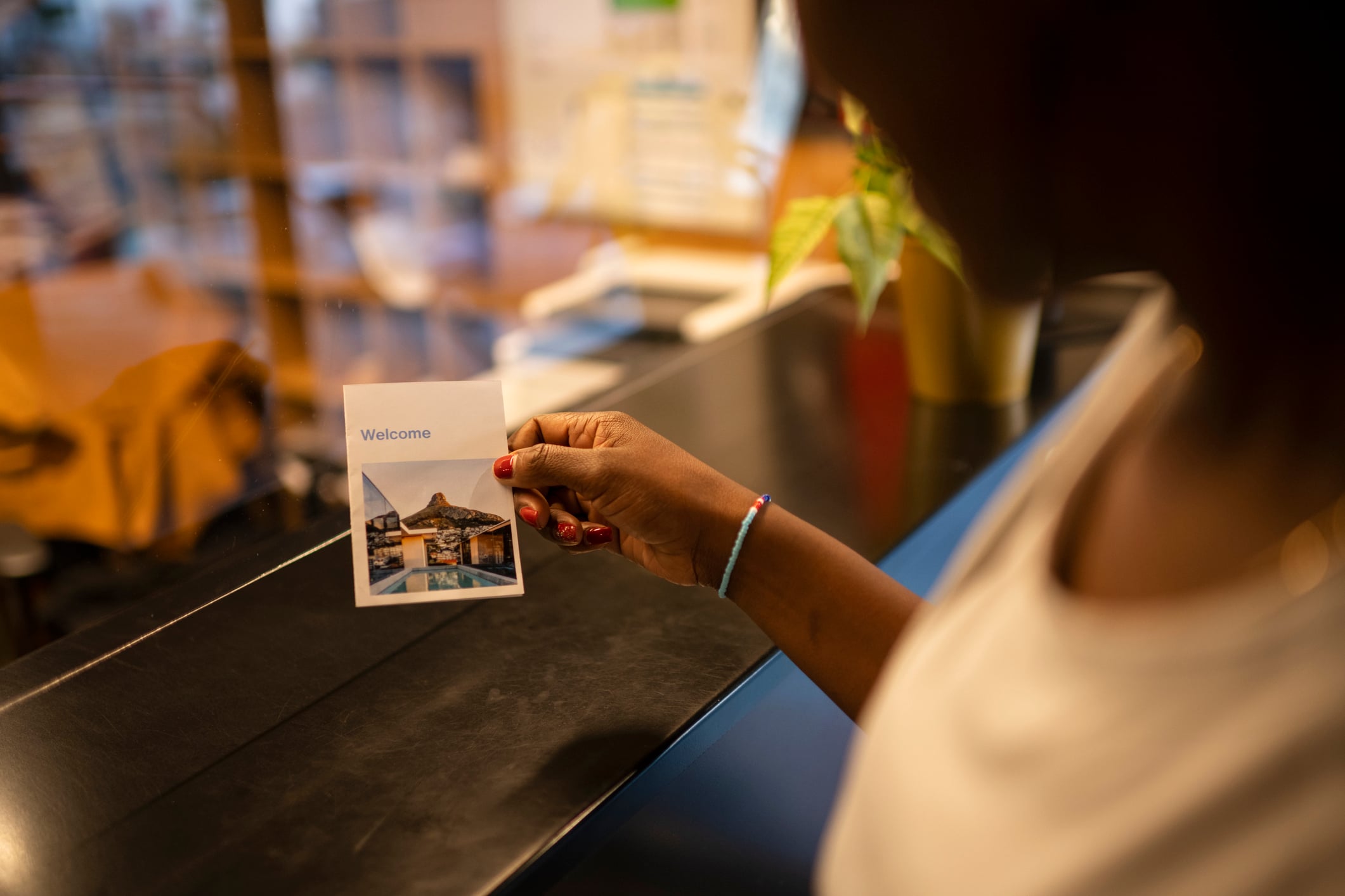 A person holds a small card that says “Welcome” above a photo of a swimming pool and a mountain.