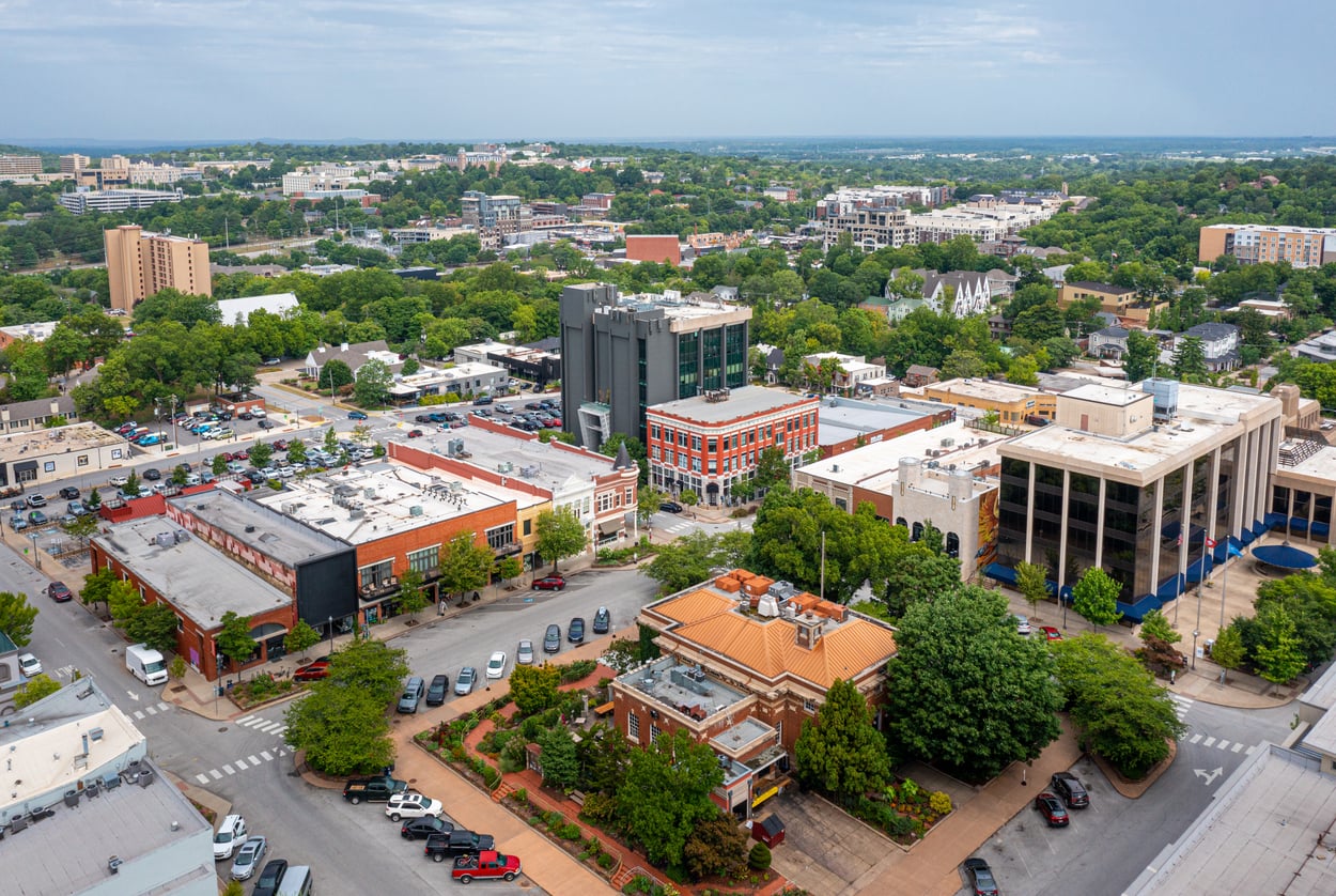 Aerial view of a town center featuring a mix of historic brick buildings, contemporary office structures, and surrounding green trees.