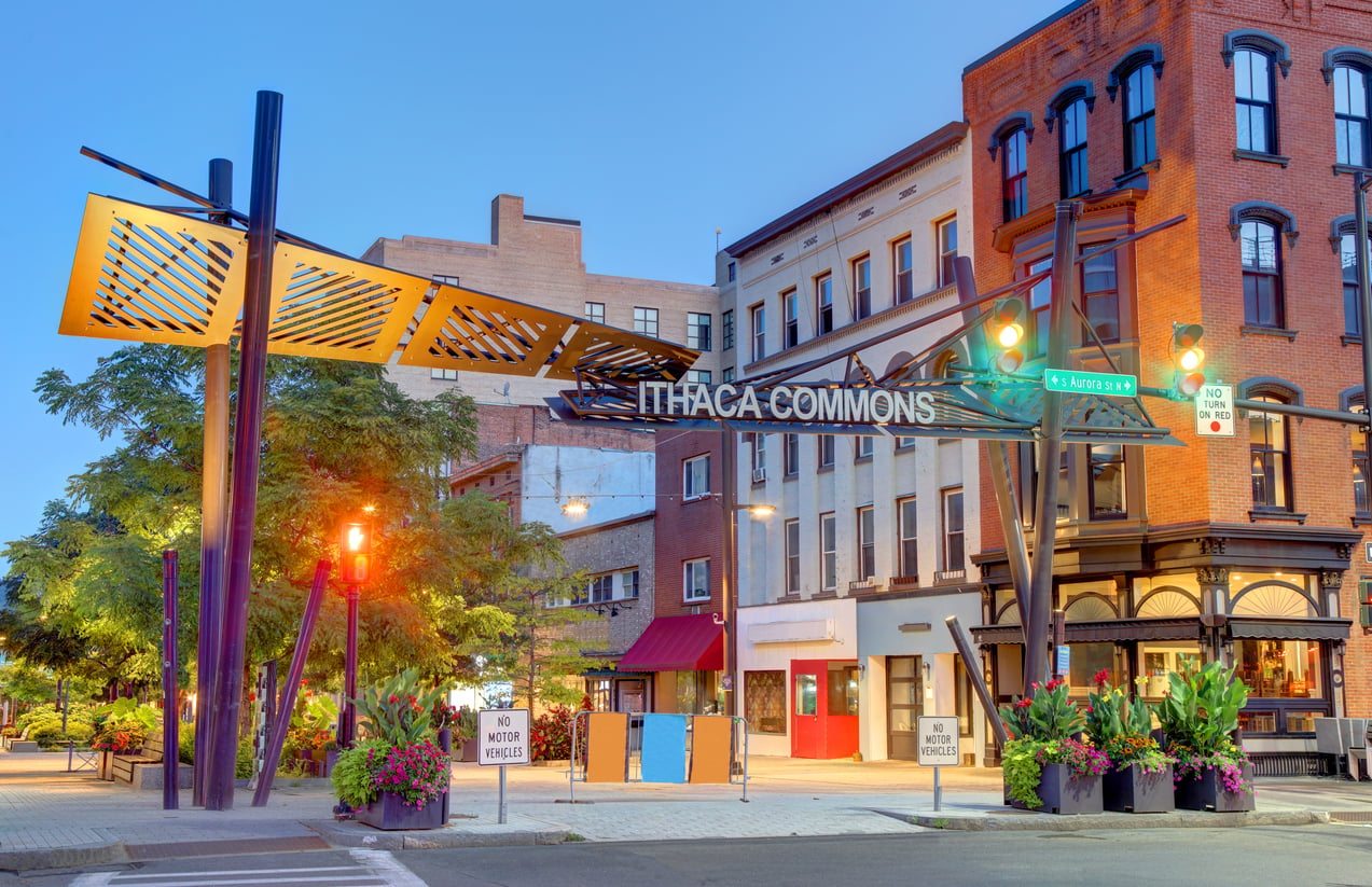An entrance archway labeled “Ithaca Commons” standing at the edge of a pedestrian street lined with historic brick buildings.