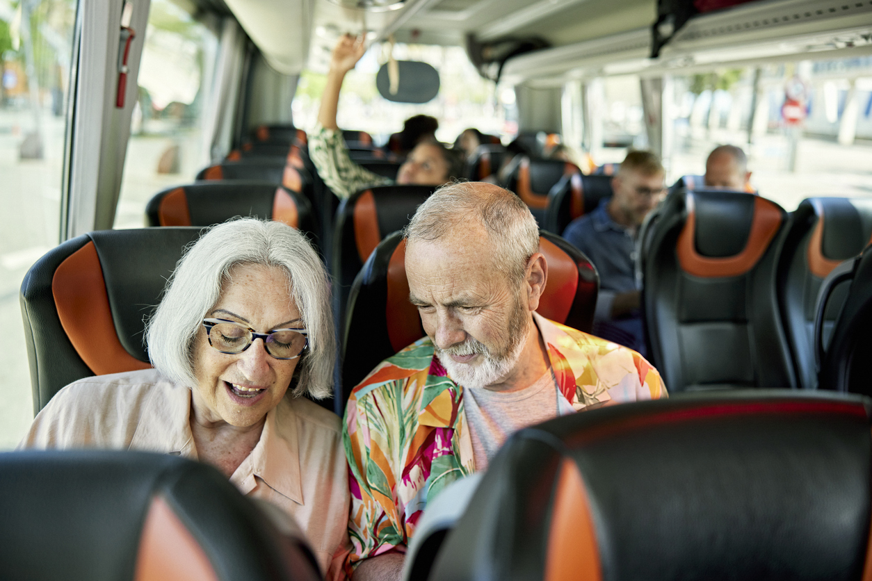 An older couple sits together in the passenger seats of a bus.