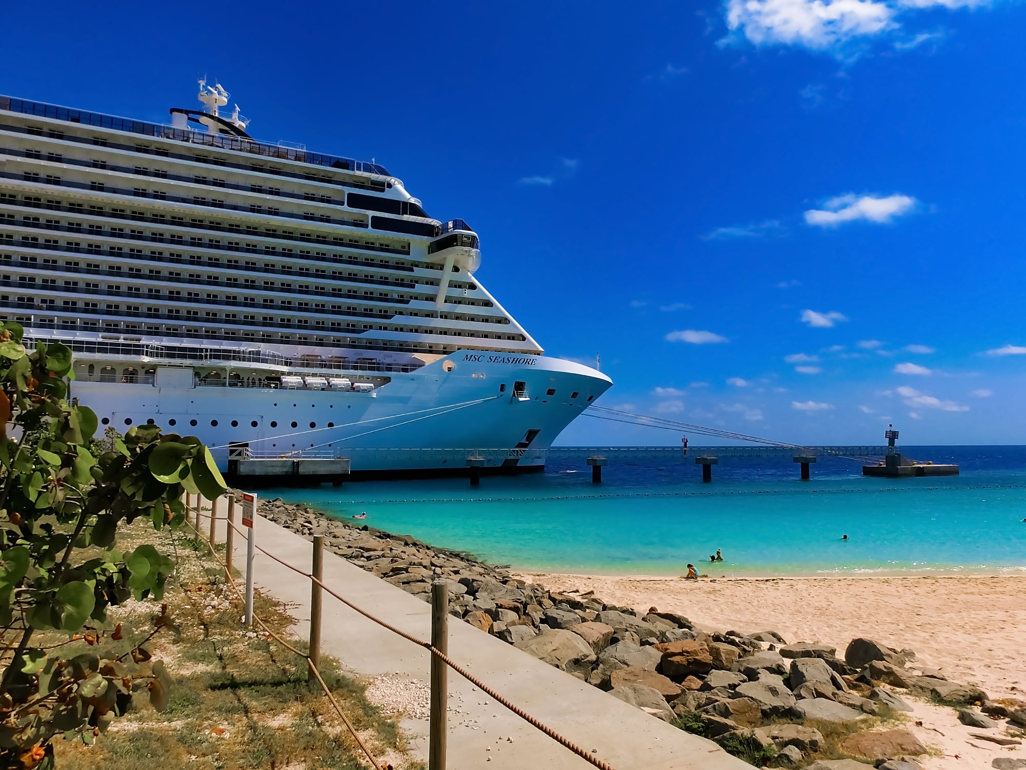 The MSC Seashore cruise ship docked at a pier extending into turquoise water above a sandy beach.
