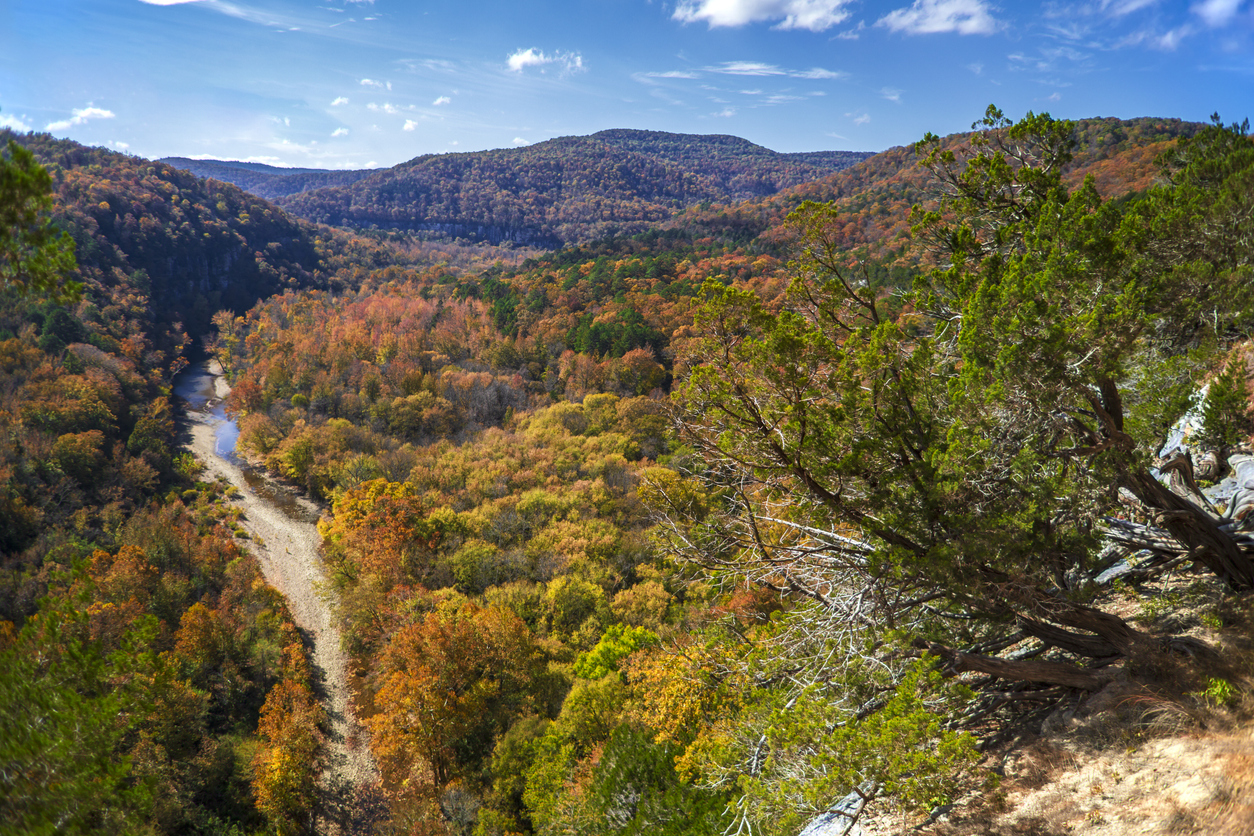 A winding river flows through a valley of dense, autumn-foliage forests, one of the many scenic places to hike in the fall.