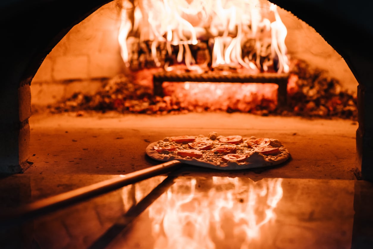 A pizza topped with tomatoes being placed into a wood-fired oven.