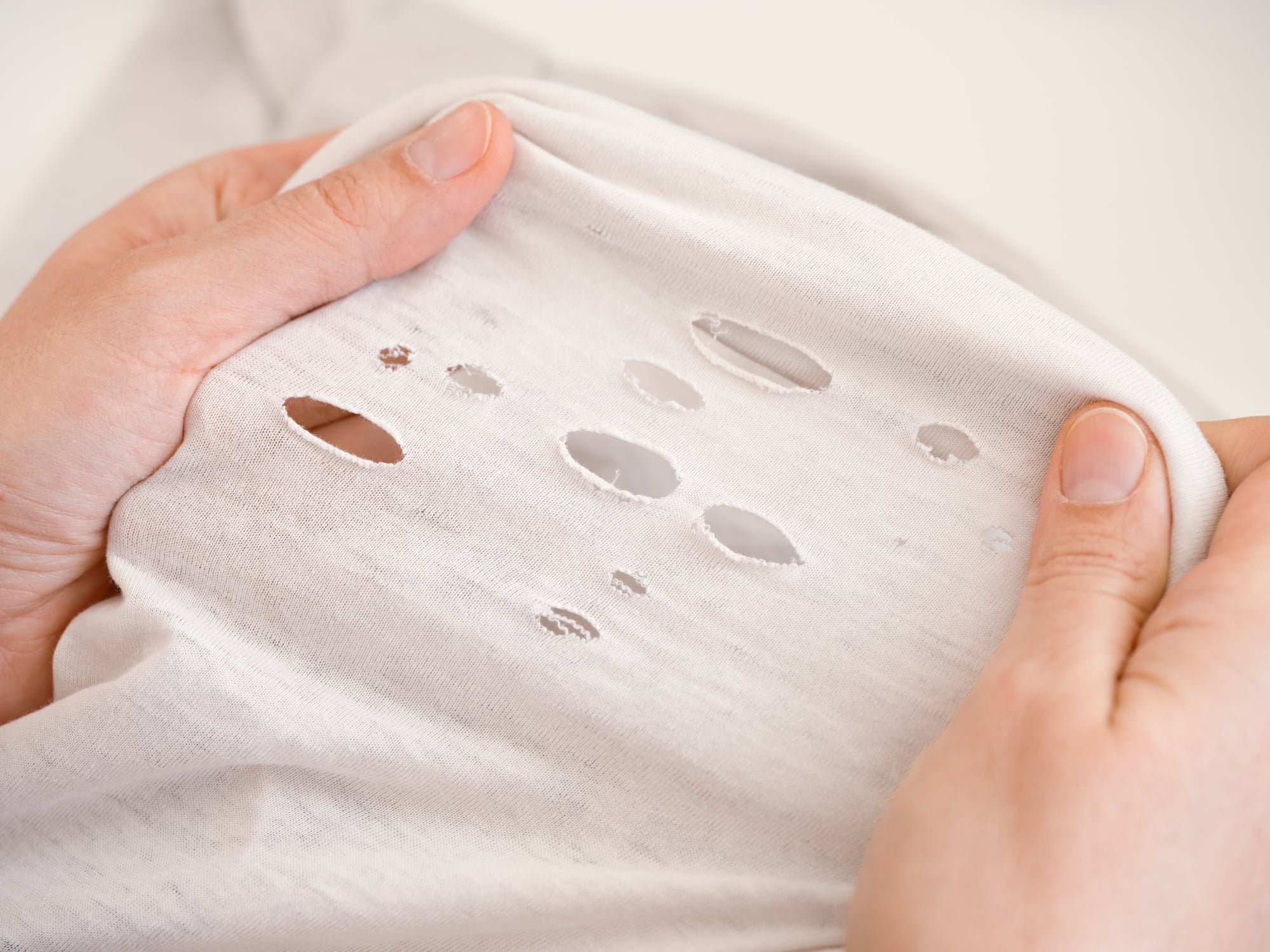 Hands holding a white fabric garment with several small holes, a reminder of the things boomers saved.