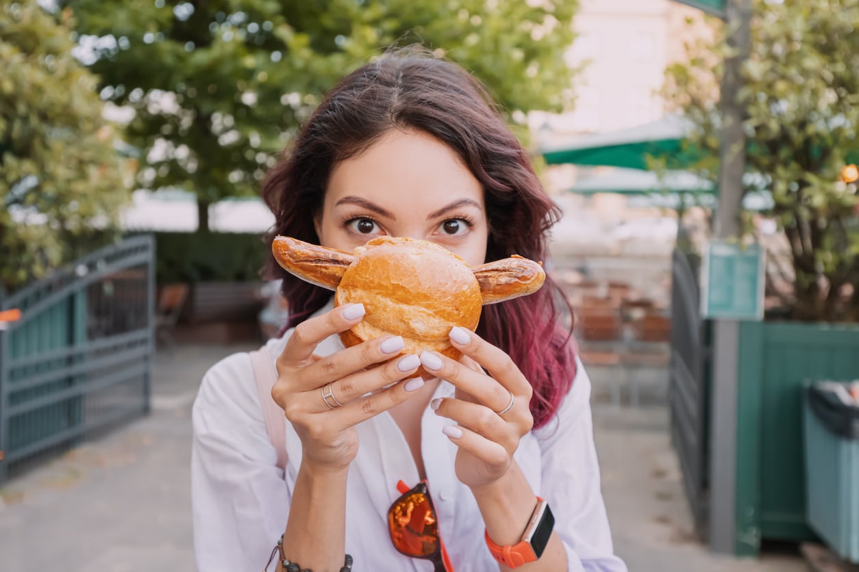A woman holds a small sandwich in front of her face, with the ends of a sausage sticking out the sides to look like a mustache.