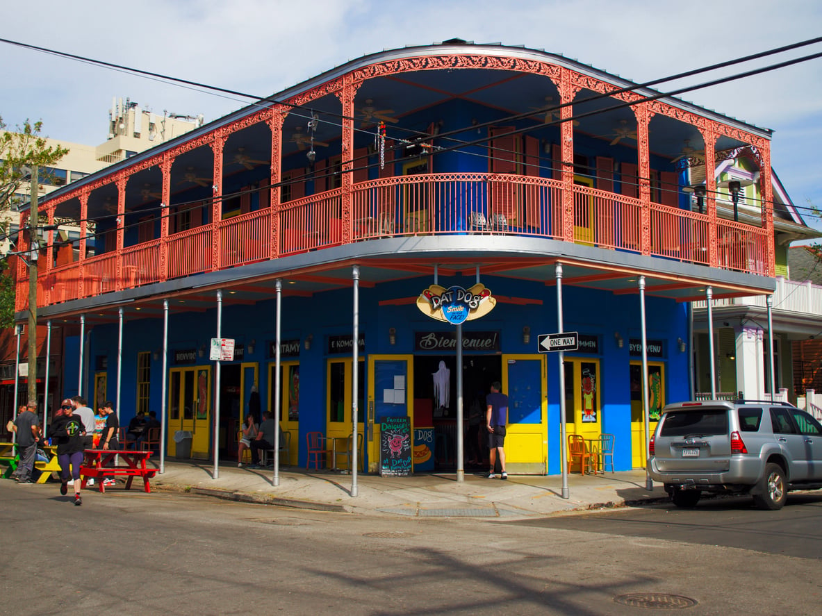 Two-story blue corner building with a red balcony and a Dat Dog restaurant sign above the entrance.