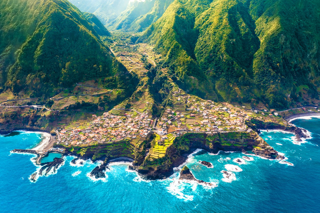 Aerial view of a coastal village nestled between steep green mountains and the blue ocean, stuff you find in European islands.