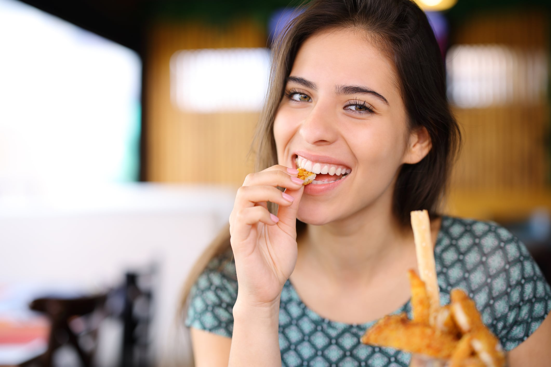 A smiling woman holding and eating a piece of fried food.