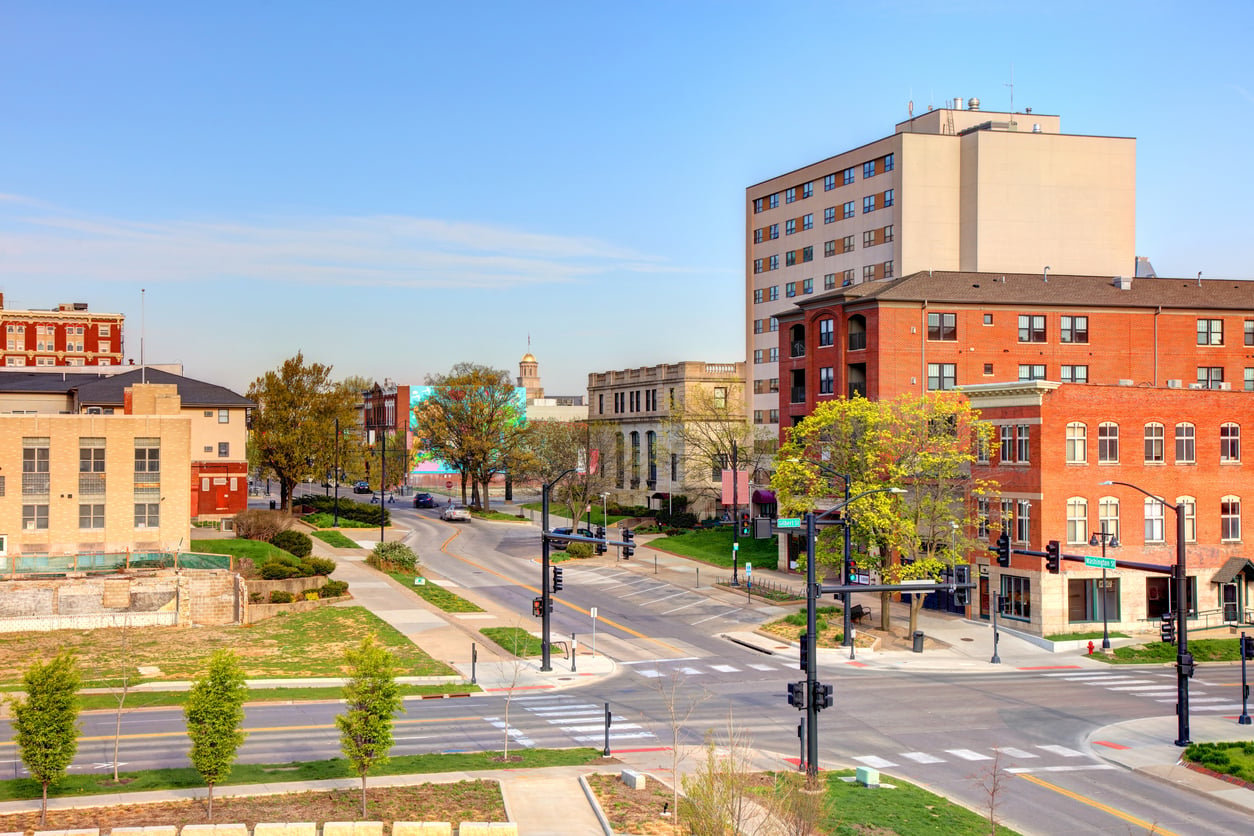 An elevated view of a city intersection with brick buildings, sparse trees, and a clear blue sky.