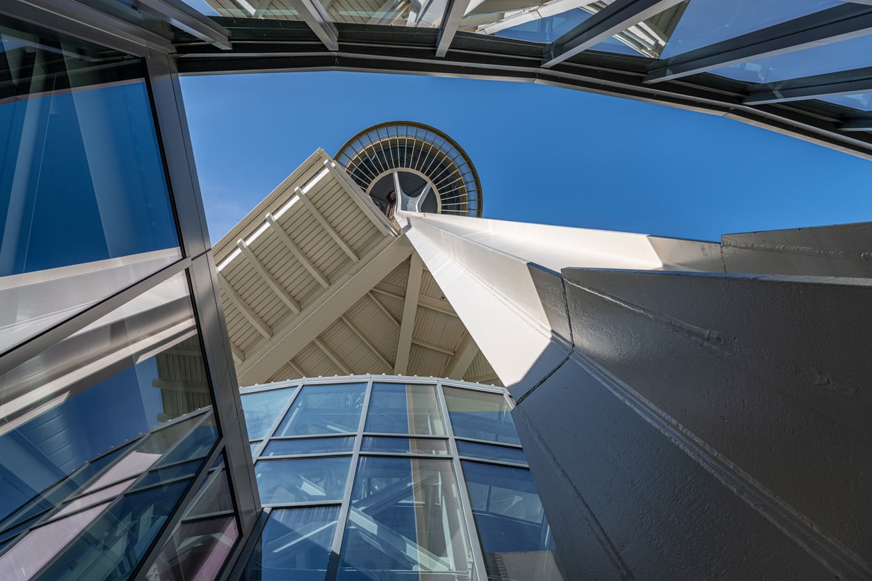 Low-angle view of the Space Needle, a iconic Seattle tourist attraction framed by modern glass panels.