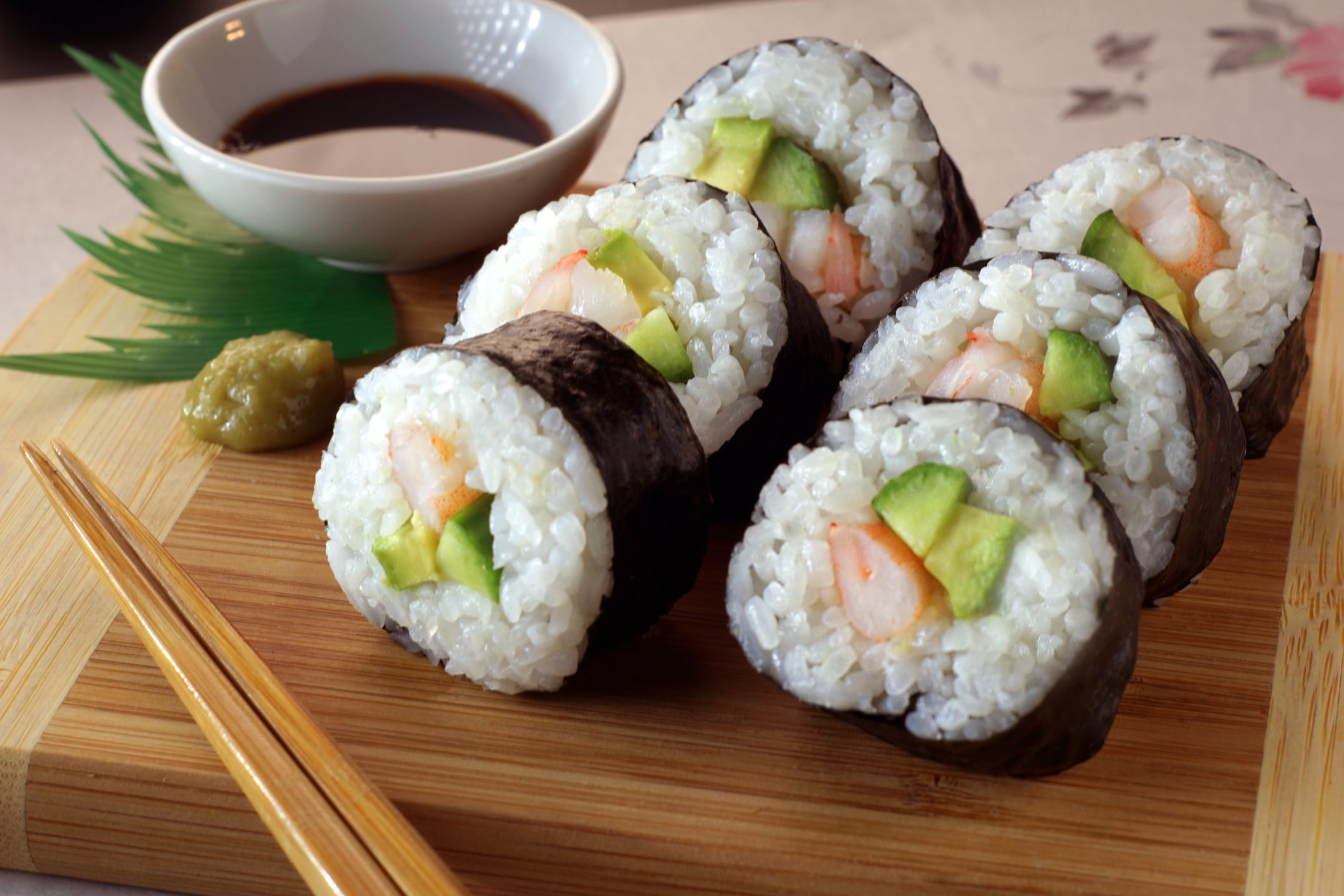 Shrimp and avocado sushi rolls on a wooden board with a side of soy sauce, wasabi, and chopsticks.