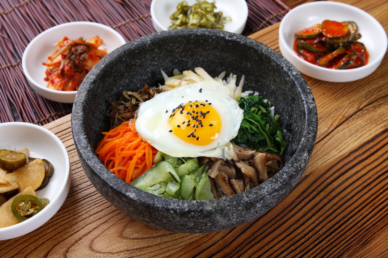 A stone bowl of bibimbap topped with a fried egg and surrounded by four small side dishes of pickled vegetables.