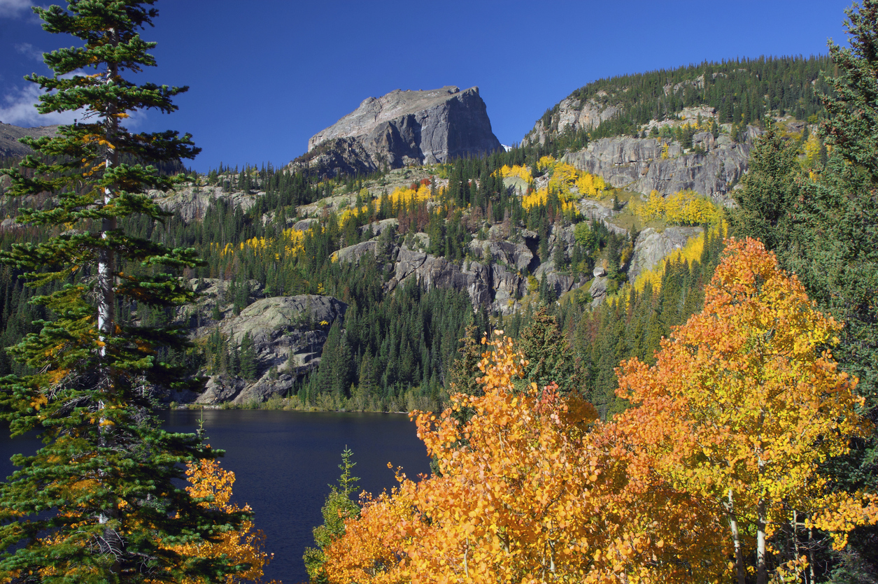 A mountain lake surrounded by evergreen forests and autumn trees with bright orange and yellow foliage, offering some of the best places to hike in the fall.