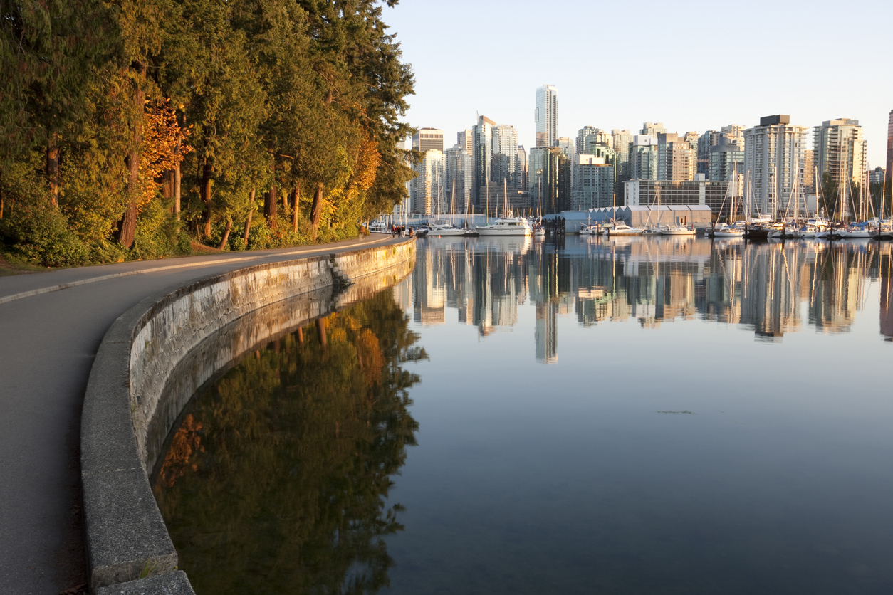 A paved walkway along a seawall next to a marina, where the Vancouver city skyline reflects in the calm water for trips that feel luxurious.