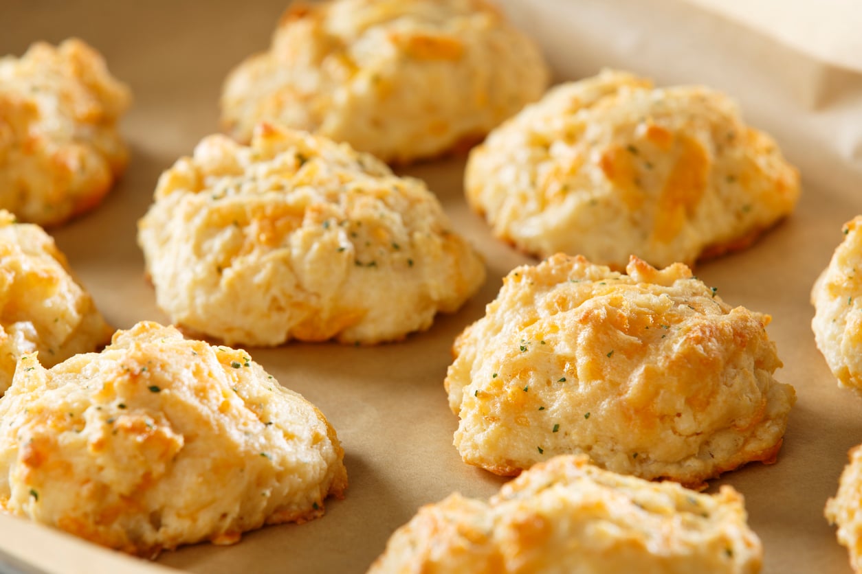 A baking sheet lined with parchment paper holds several golden-brown cheddar herb drop biscuits.