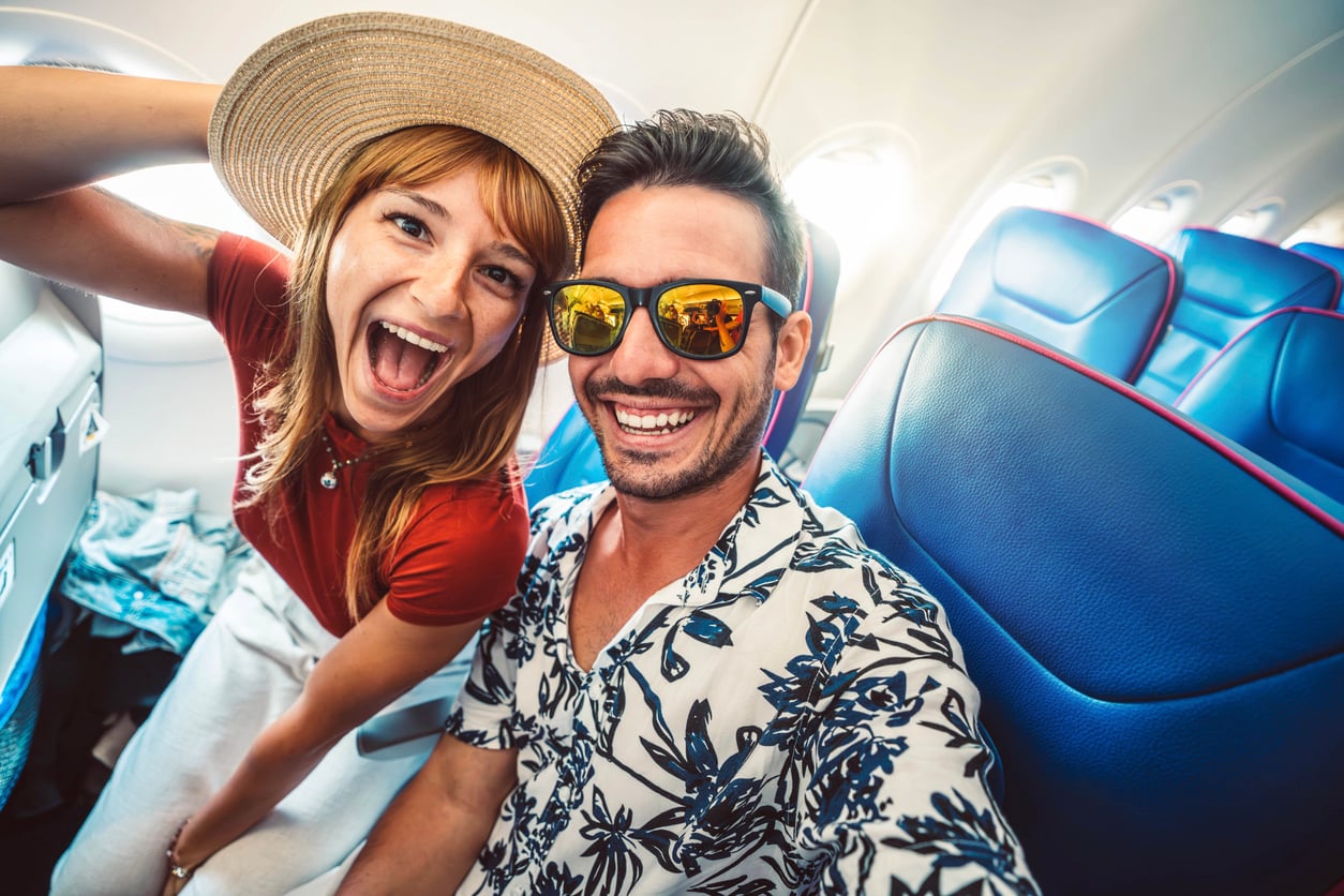 A smiling man and woman in a sun hat take a selfie in their airplane seats.