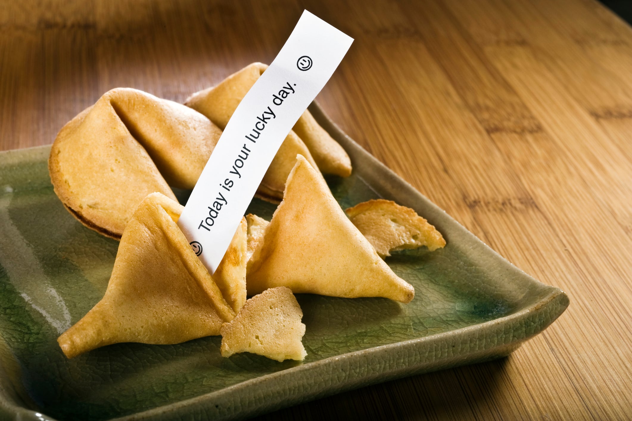Fortune cookies on a green square plate, with one cookie holding a paper slip that reads, “Today is your lucky day.”