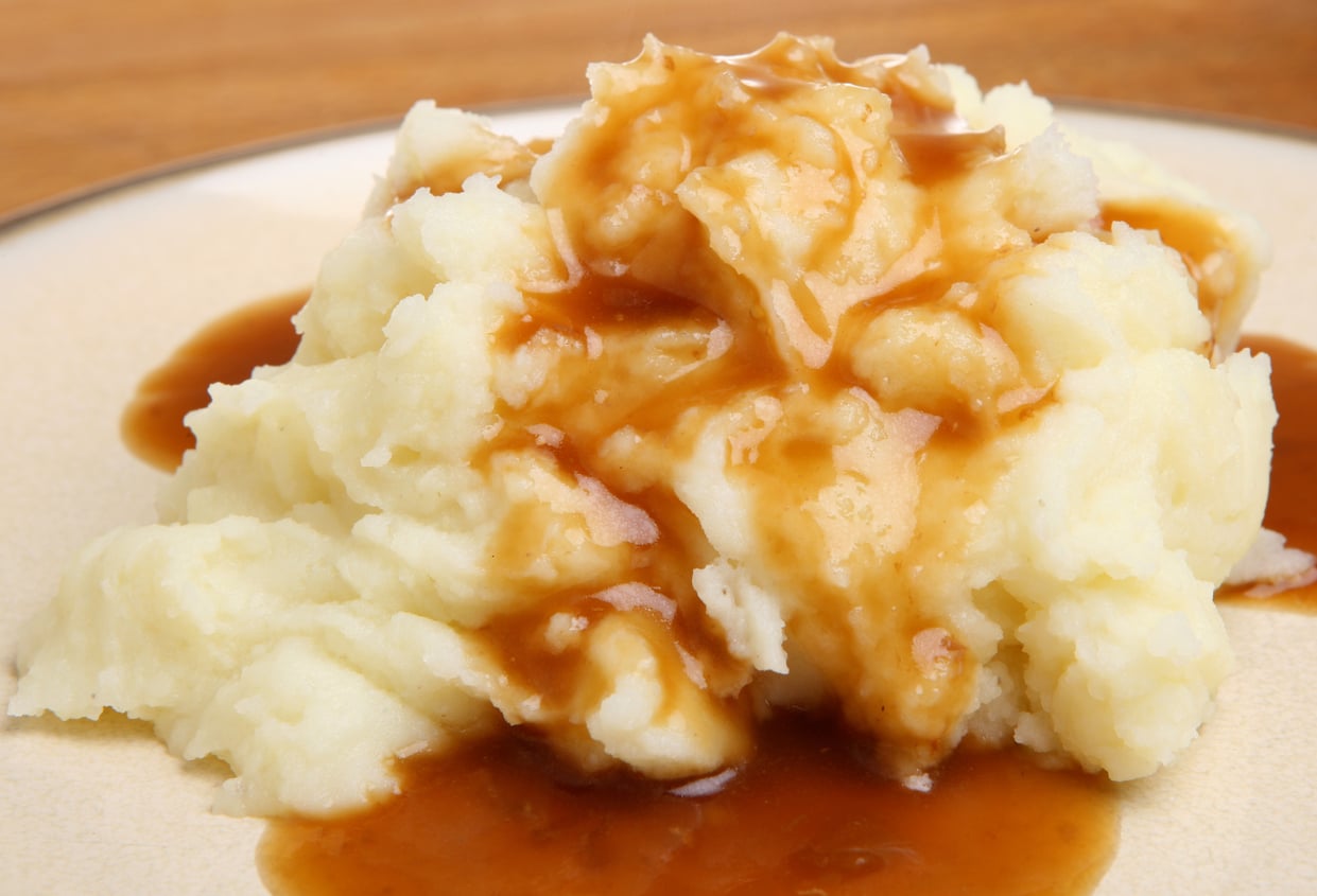 A mound of mashed potatoes topped with brown gravy on a plate.