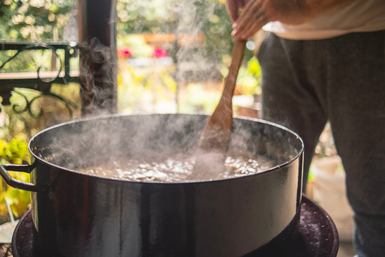 A person stirs a large pot of steaming food with a wooden spoon.