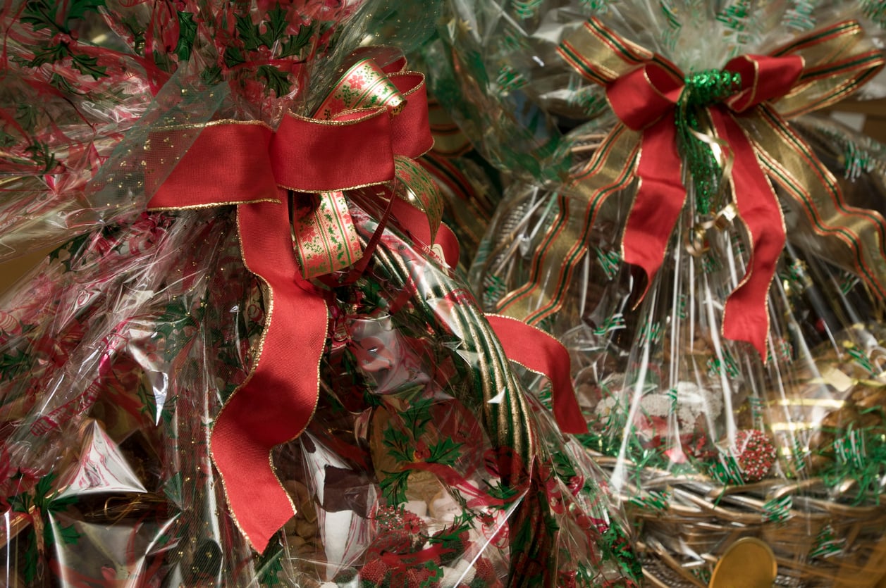 Two gift baskets wrapped in clear plastic with festive holiday patterns and topped with large red bows.
